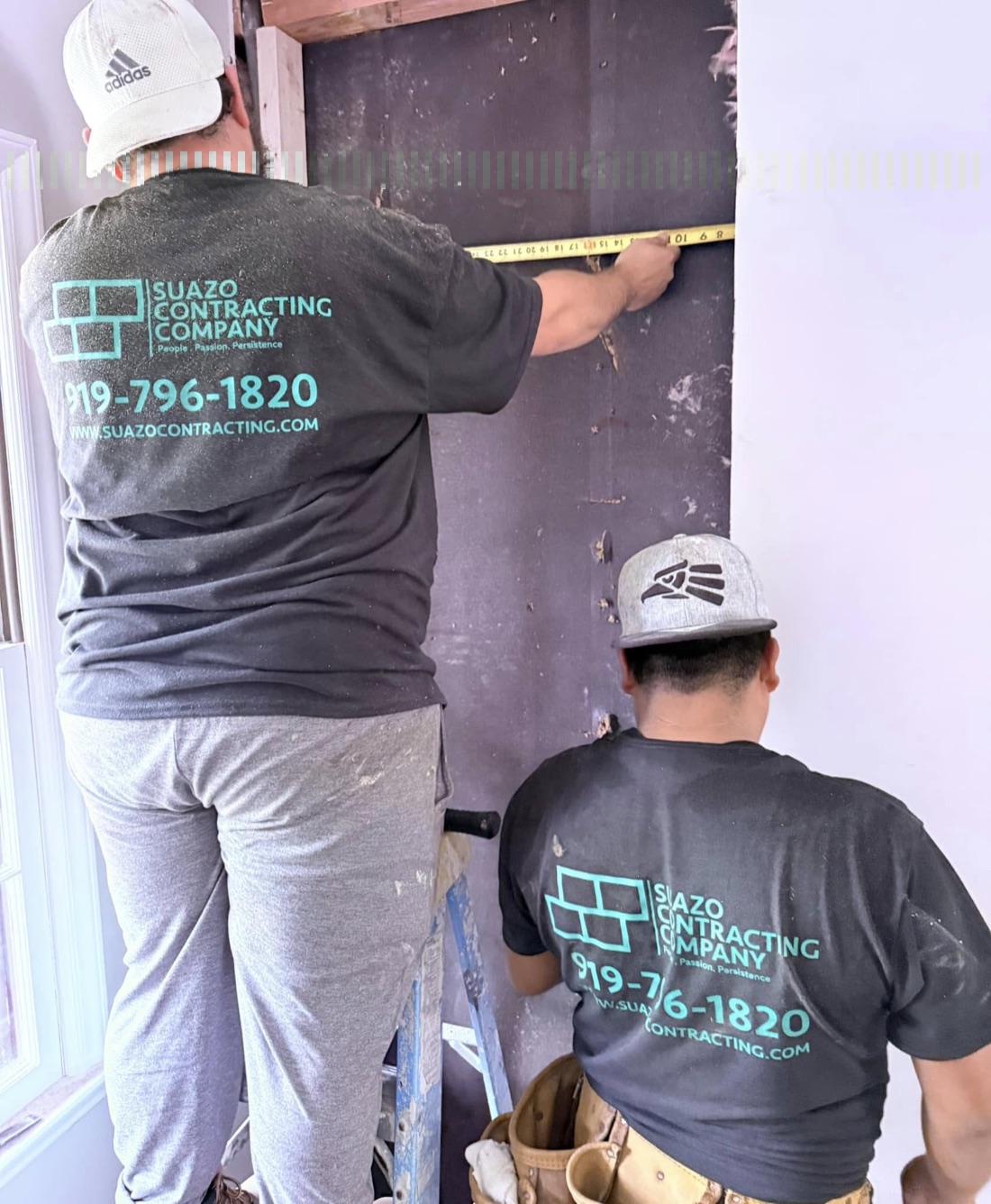 Two Suazo Contracting crew members in company shirts measuring a wall on a job